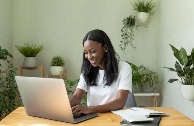 Femme souriante travaillant sur un ordinateur portable dans un environnement verdoyant.