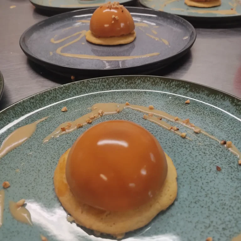 Dessert sphérique en caramel sur un biscuit, décoré de sauce.