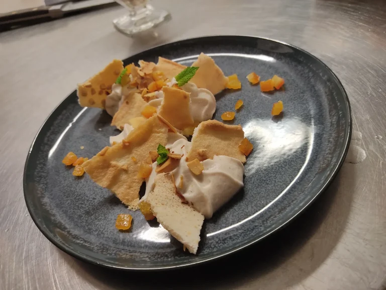 Dessert élégant avec des morceaux de meringue et de la crème sur une assiette noire.