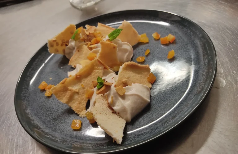 Dessert composé de morceaux de meringue, crème et éclats de fruits sur une assiette noire.