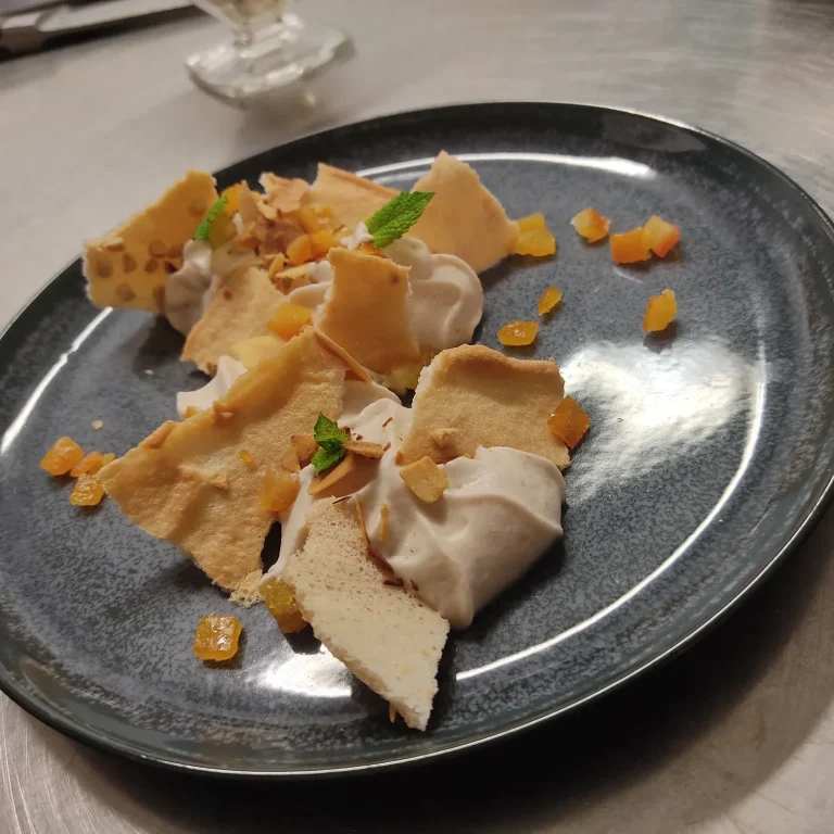 Dessert composé de crêpes, crème, morceaux de fruits et d'amandes sur une assiette noire.