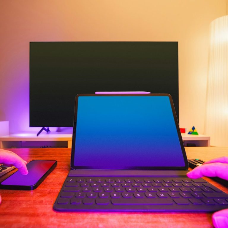 Bureau avec un ordinateur portable, un téléphone et un téléviseur en arrière-plan éclairé.