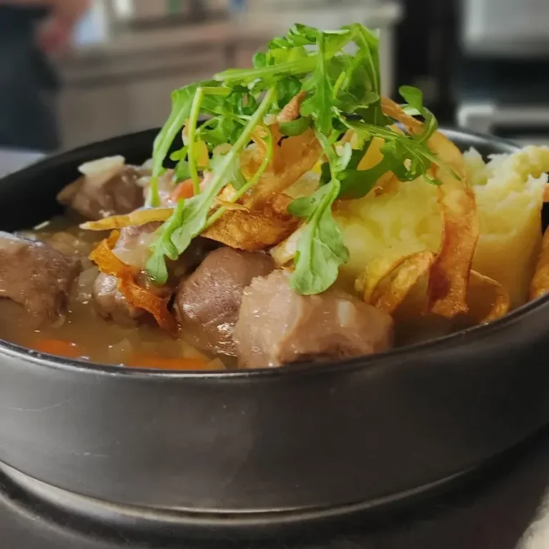 Plat de viande en sauce, accompagné de légumes et de purée, garni de roquette.